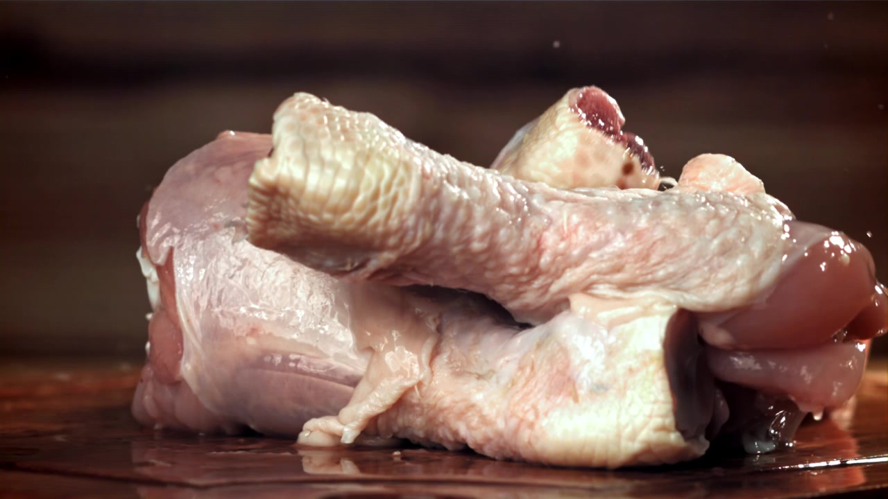 Fusi di pollo crudi e freschi che cadono su una superficie di legno bagnata al rallentatore