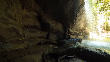 pov inside cave looking out to lagoon and waterfall in rainforest on sunny day