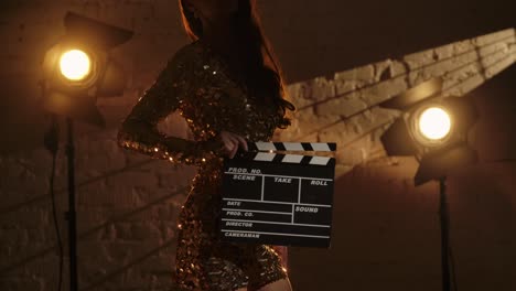 woman in gold dress holding a clapperboard