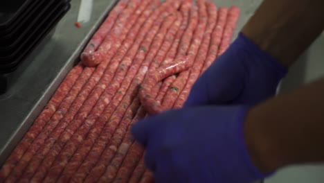 Butcher-stuffing-endless-line-of-sausages-wearing-blue-gloves,-close-up