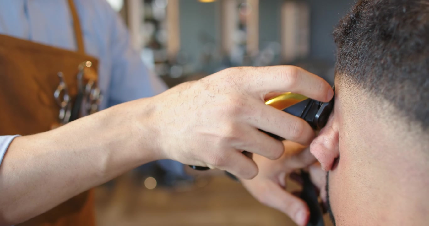 Barbeiro afro-americano aparando o cabelo do cliente com máquina perto da orelha na barbearia, fazendo um corte degradê para harmonizar a linha do cabelo