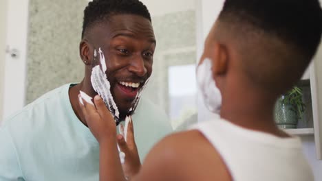Afroamerikanischer-Junge,-Der-Seinem-Vater-Rasierschaum-Ins-Gesicht-Schmiert-Und-Gemeinsam-Lacht
