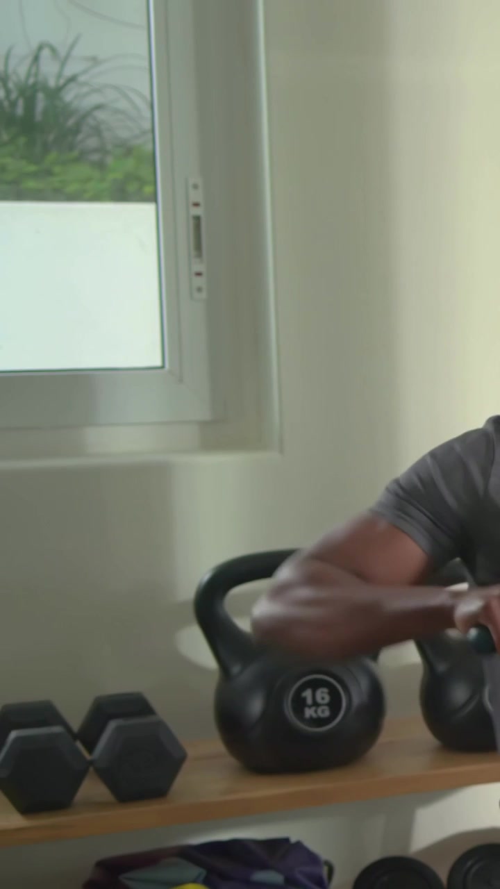 Vertical video: Reaching man in gym kit grasping rower grip pulling to train at home, copy space
