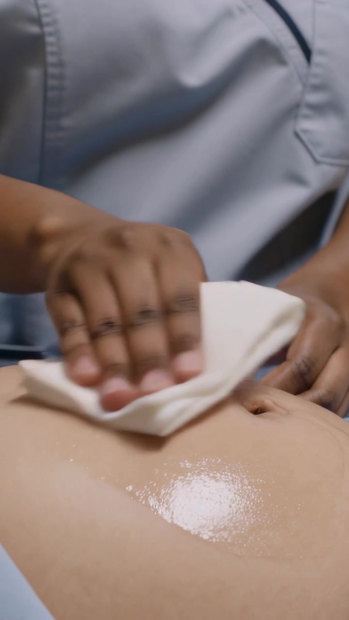 Video verticale: Infermiera in divisa che pulisce rimuovendo il gel dal busto del paziente in clinica dopo un esame, con un panno