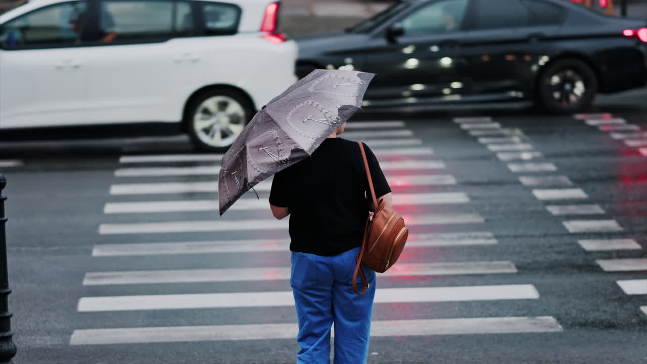 Woman holding an umbrella waiting at a pedestrian crossing on a rainy day in Chisinau, Moldova