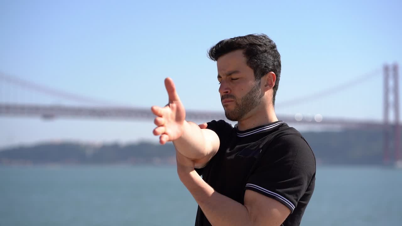 joven deportista enfocado estirando los brazos a la orilla del río
