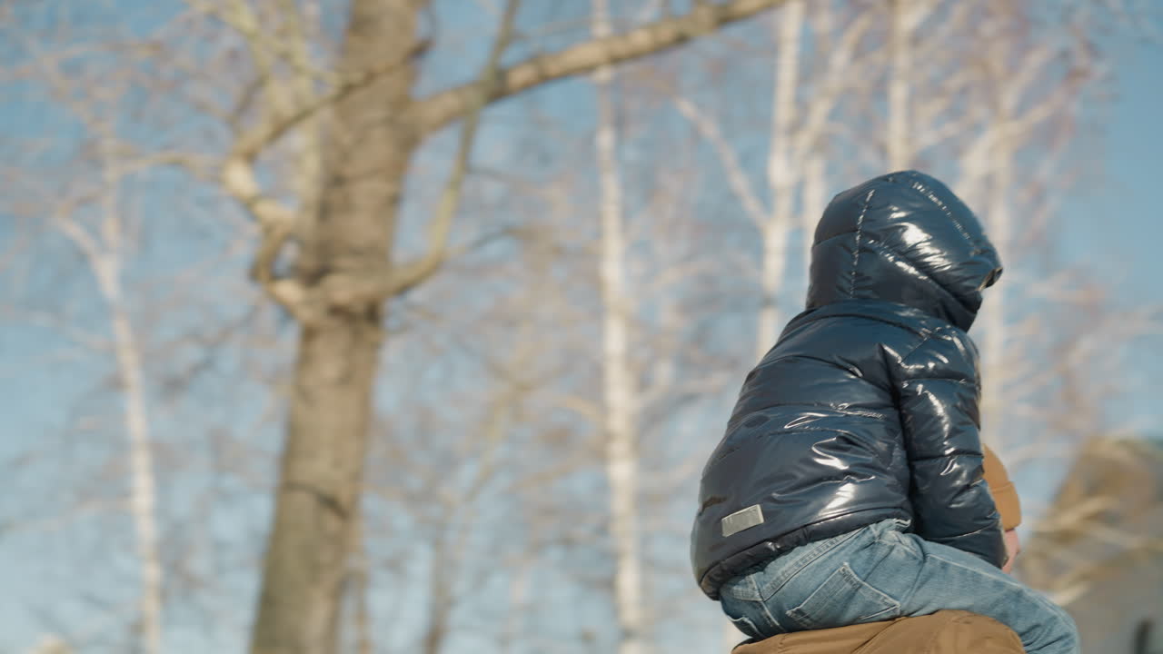 아들을 어깨에 고 있는 아버지의 회전적인 모습, 그의 눈은 베니로 여 있으며, 그들은 행복하게 움직이고, 에는 조명 기둥이 있습니다.