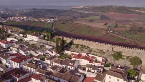 Side-panning-shot-of-old-city-wall-of-Obidos-Portugal-during-morning,-aerial