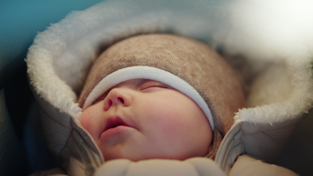 Nærbillede af en sovende baby svøbt i varmt vintertøj med blødt naturligt lys