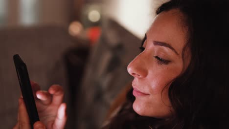 Young-Italian-woman-using-a-smart-phone-scrolling-while-sat-on-the-sofa-at-home