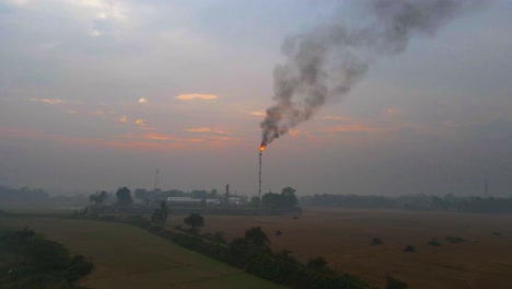 the sun sets behind a gas plant, with burning gases in the chimney, evoking a dystopian end-of-the-world concept