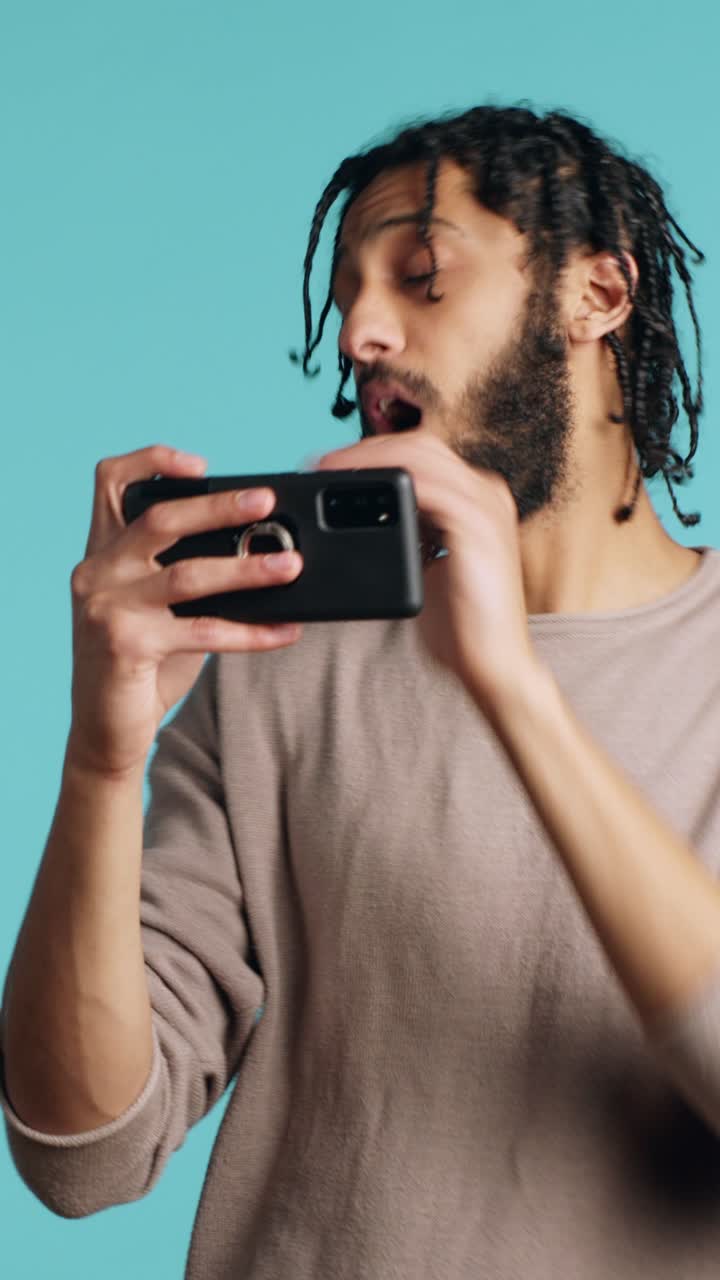 Vertical video Man nodding head, upset after losing videogame, playing on phone in studio