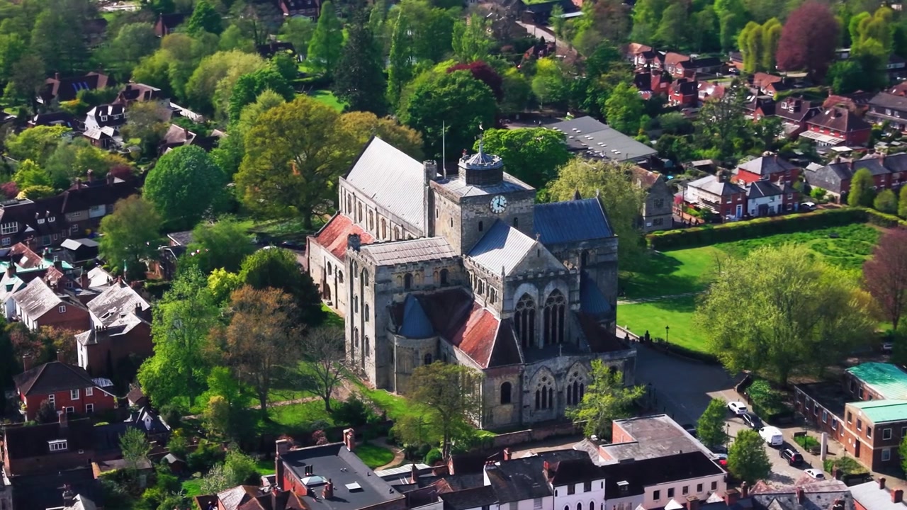 Droneoptagelser fra luften af Romsey Abbey i Hampshire, der viser den historiske klosterkirke omgivet af træer, grønne områder, hustage, gader og det nærliggende landskab på en solrig dag. Nyttigt for britiske.