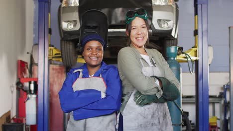 video of two diverse happy female car mechanics posing at camera