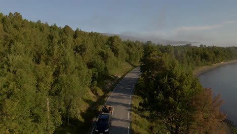 Car-driving-through-forested-tree-lane-in-countryside,-next-to-lake