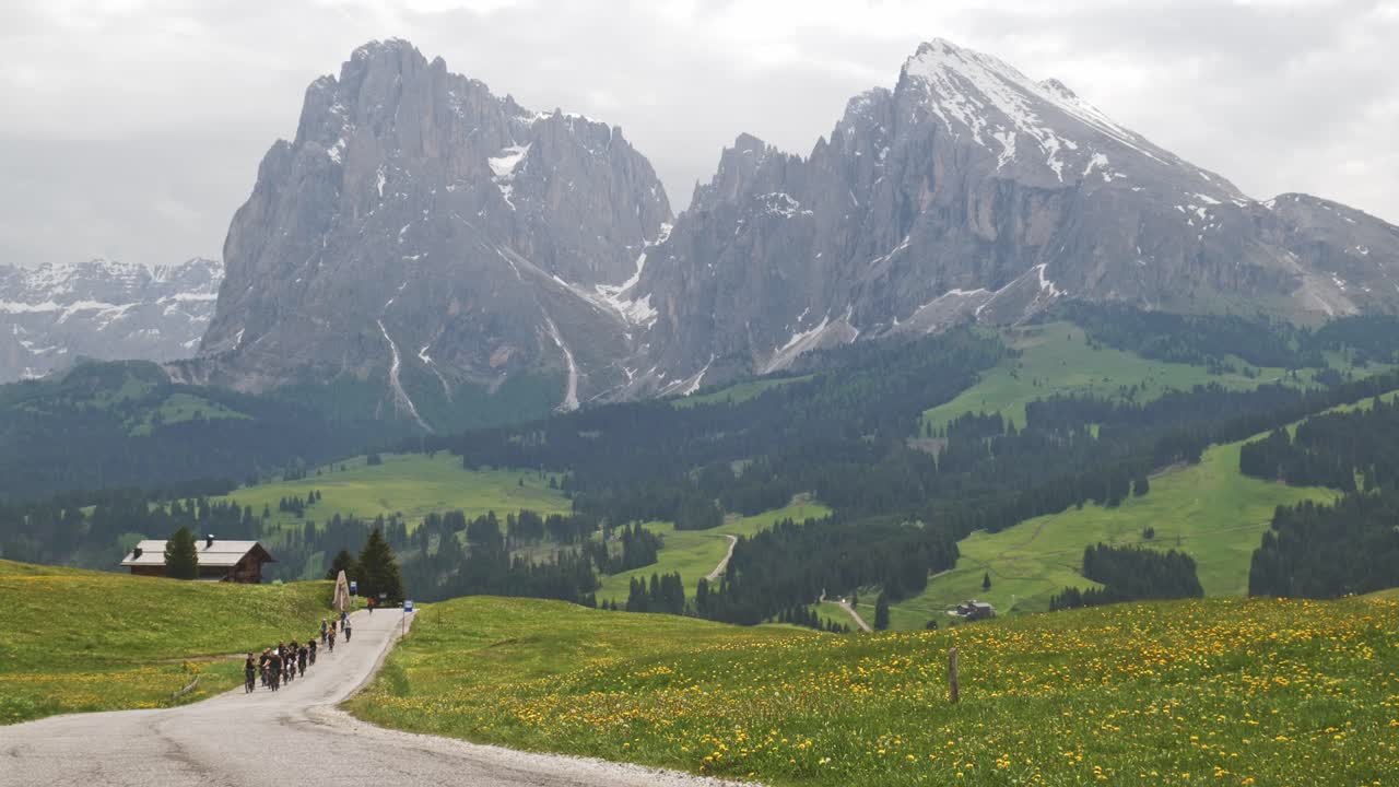 Tourist Cycling Group riding uphill in alpine meadow mountain landscape