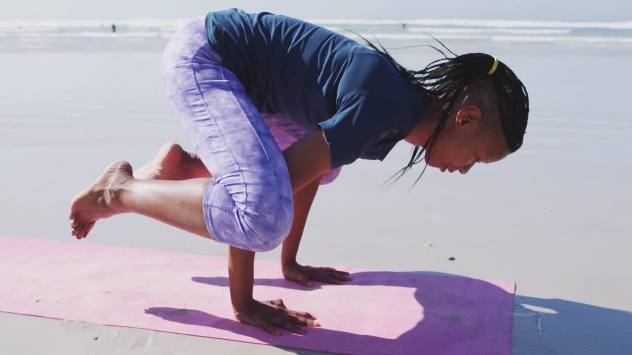 African American woman doing yoga position on the beach and blue sky background