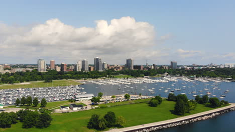 Amplia-Vista-Aérea-De-Los-Veleros-En-Una-Bahía-Tranquila-Con-El-Horizonte-De-La-Ciudad-En-El-Fondo