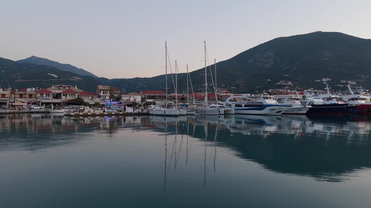 Avvicinamento a bassa quota con drone sopra acqua calma verso yacht ormeggiati nel porto turistico di Nidri durante una mattinata tranquilla a Lefkada, Grecia.
