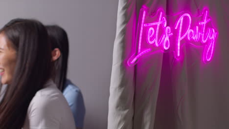 dos amigas se divierten en una cabina de fotos con un letrero de neón "vamos a festejar" afuera