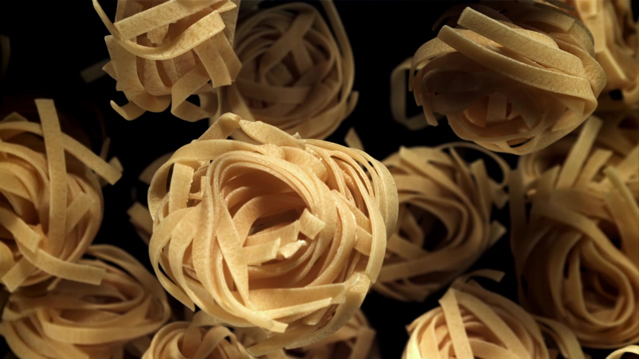 Nidi di tagliatelle secche che cadono al rallentatore su sfondo nero