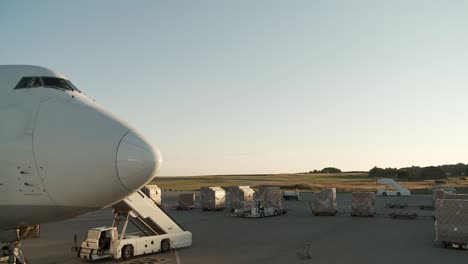 Close-up-airplane-nose-with-cockpit-window-in-sunrise,-cargo-container-loading