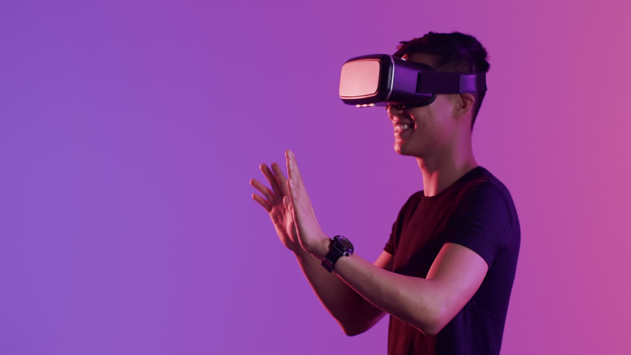 Asian man using vr headset, touching virtual screen on purple background, copy space, slow motion