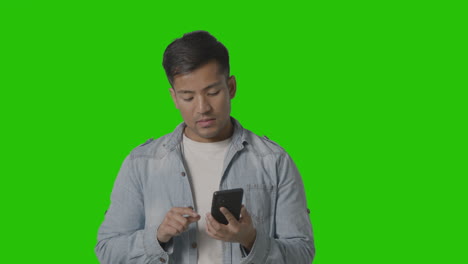 Studio-Shot-Of-Casually-Dressed-Young-Man-Online-Swiping-On-Mobile-Phone-Against-Green-Screen-2