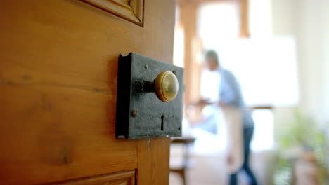 Door-over-senior-biracial-woman-wearing-apron-and-painting-on-big-canvas-at-home,-slow-motion