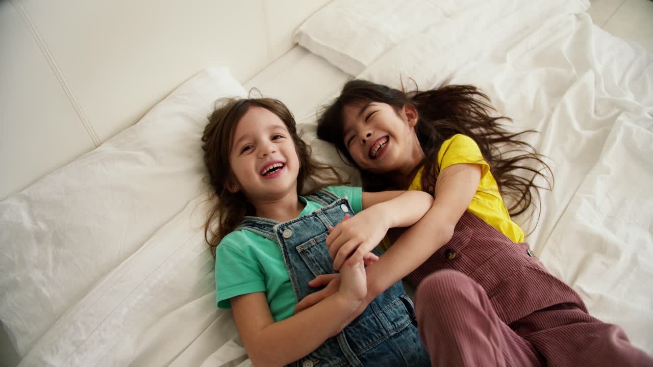 Girl, friends or children on white bed while relax together and play, top view