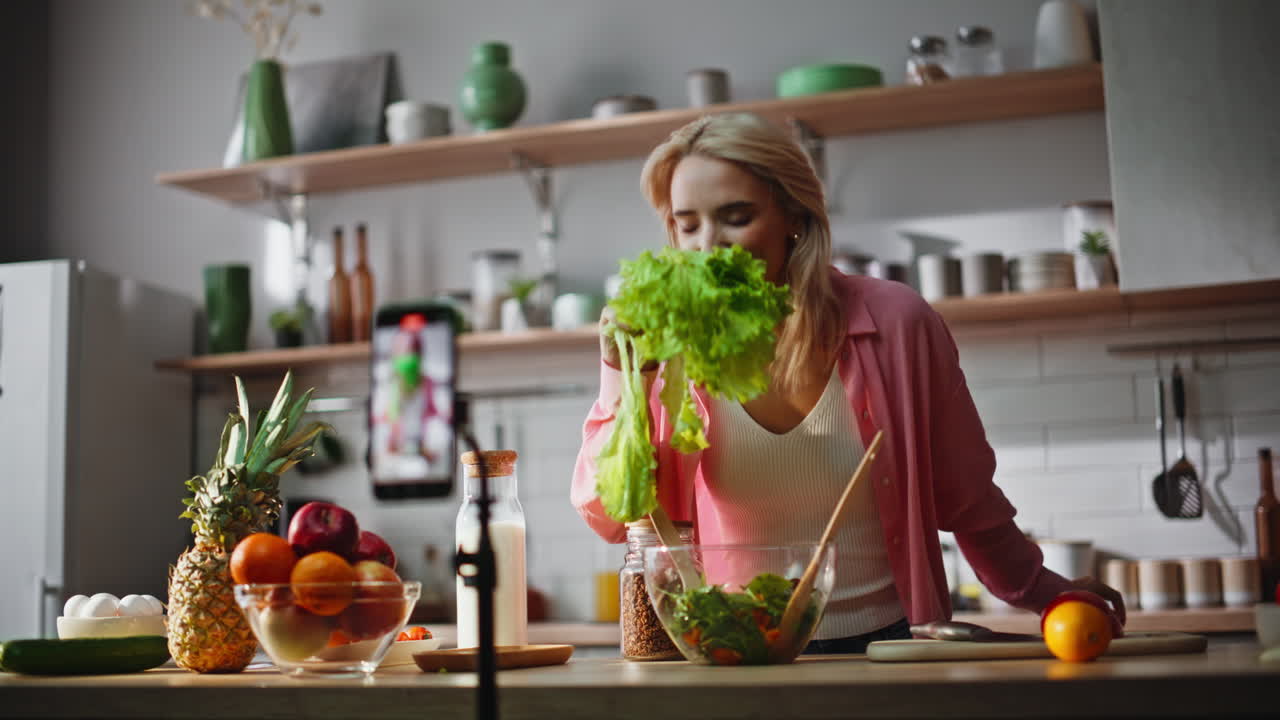 Blonde recording food blog talking smartphone camera at light kitchen closeup