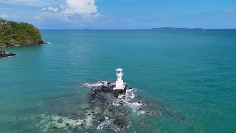 drone footage captures a serene lighthouse on a tropical bluff in phuket, thailand, surrounded by turquoise waters and lush greenery