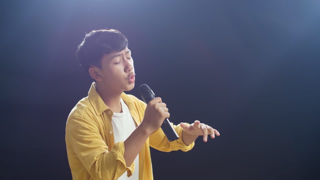 젊은 아시아 소년 이 마이크 를 들고 검은 바탕 에  을 하고 있다