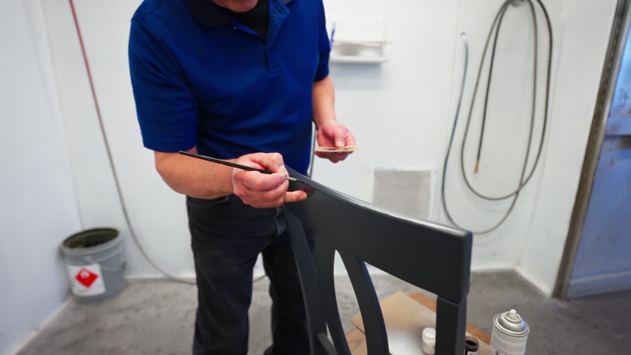 Close gimbal move shows man painting grey wooden chair corner in spray booth