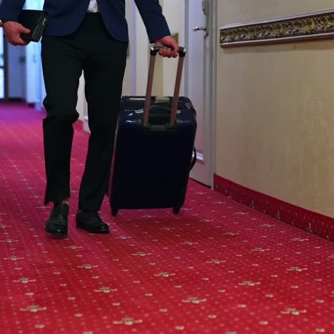 unrecognizable businessman with luggage in a hotel corridor. a man with a suitcase is walking down a hotel hallway