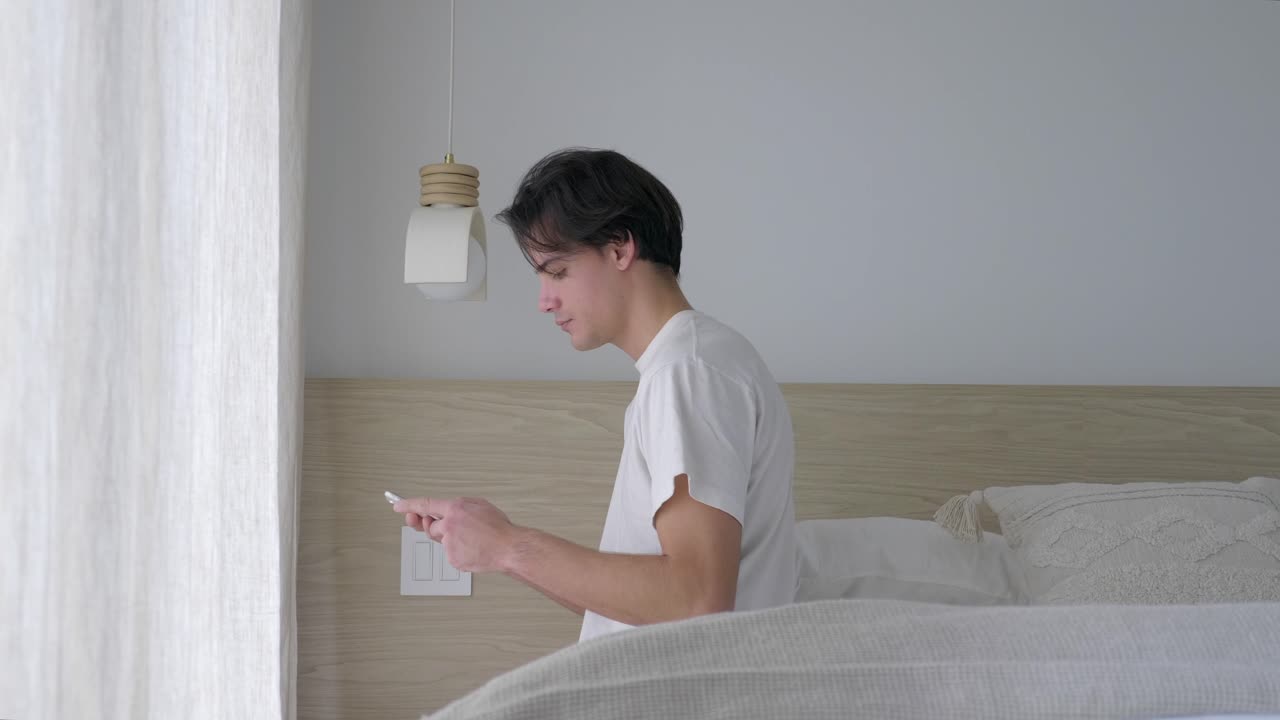 남자 는 침대 에 앉아서 휴대 전화 에 메시지 를 입력 한다