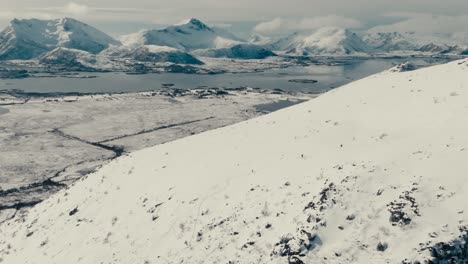 hikers on steep mountains covered with snow in gimsoya island, vagan, nordland county, norway. aerial drone shot