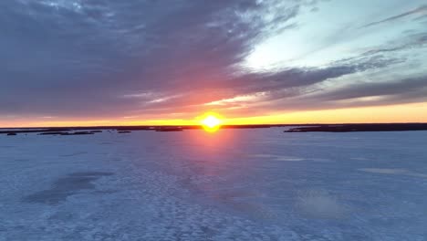 Drone-flight-over-a-frozen-lake-and-clouds-at-sunset