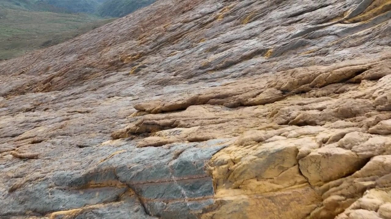 Vista em ângulo baixo ao longo de uma face rochosa íngreme mostrando camadas de arenito texturizadas, planos de estratificação contínuos, protuberâncias arredondadas e desgastadas, rachaduras finas e tons de azul acinzentado frio a ocre quente