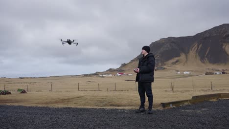 piloto de dron en carretera de grava negra usa el control remoto para volar hacia la montaña