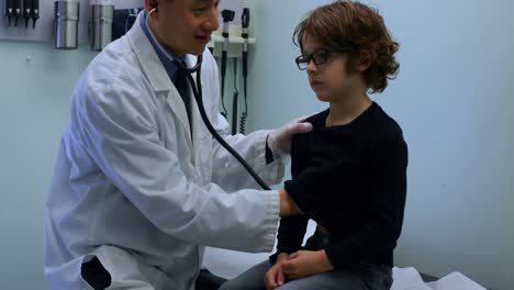 Side-view-of-young-asian-male-doctor-examining-caucasian-boy-patient-chest-in-a-clinic-4k