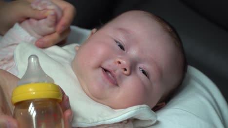 happy newborn infant baby girl smile to the camera after drinking formula milk from the bottle close up