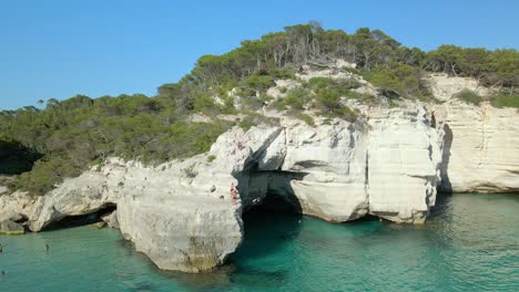 People-Jumping-Off-Huge-Limestone-Cliff-In-Cala-Mitjana,-Menorca