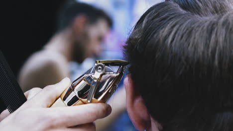 Friseur-Schneidet-Mann-Mit-Goldener-Maschine-Im-Salon-Die-Haare