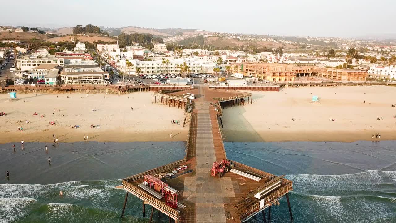 Avance aéreo sobre el muelle de madera de Pismo y gente en la playa de arena, California.