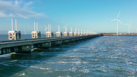 Toma-Aérea-En-Cámara-Lenta-De-Una-Barrera-De-Marejada-Ciclónica-Abierta-Del-Este-De-Scheldt-Y-Turbinas-Eólicas-En-La-Distancia-En-Zelanda,-Los-Países-Bajos-En-Un-Hermoso-Día-Soleado