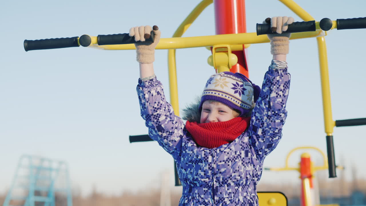 una niña con ropa abrigada está jugando en el patio de la escuela montando un entrenador de fitness