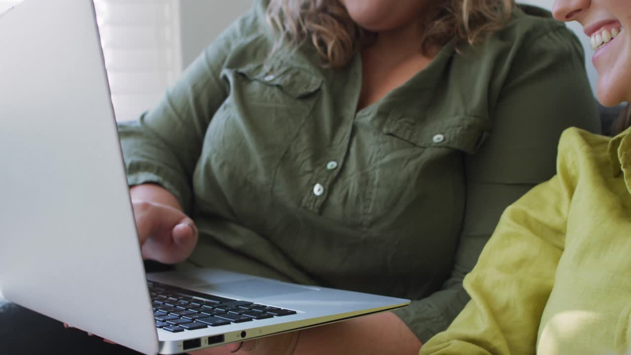 pareja de lesbianas caucásicas usando una computadora portátil y sentadas en el sofá