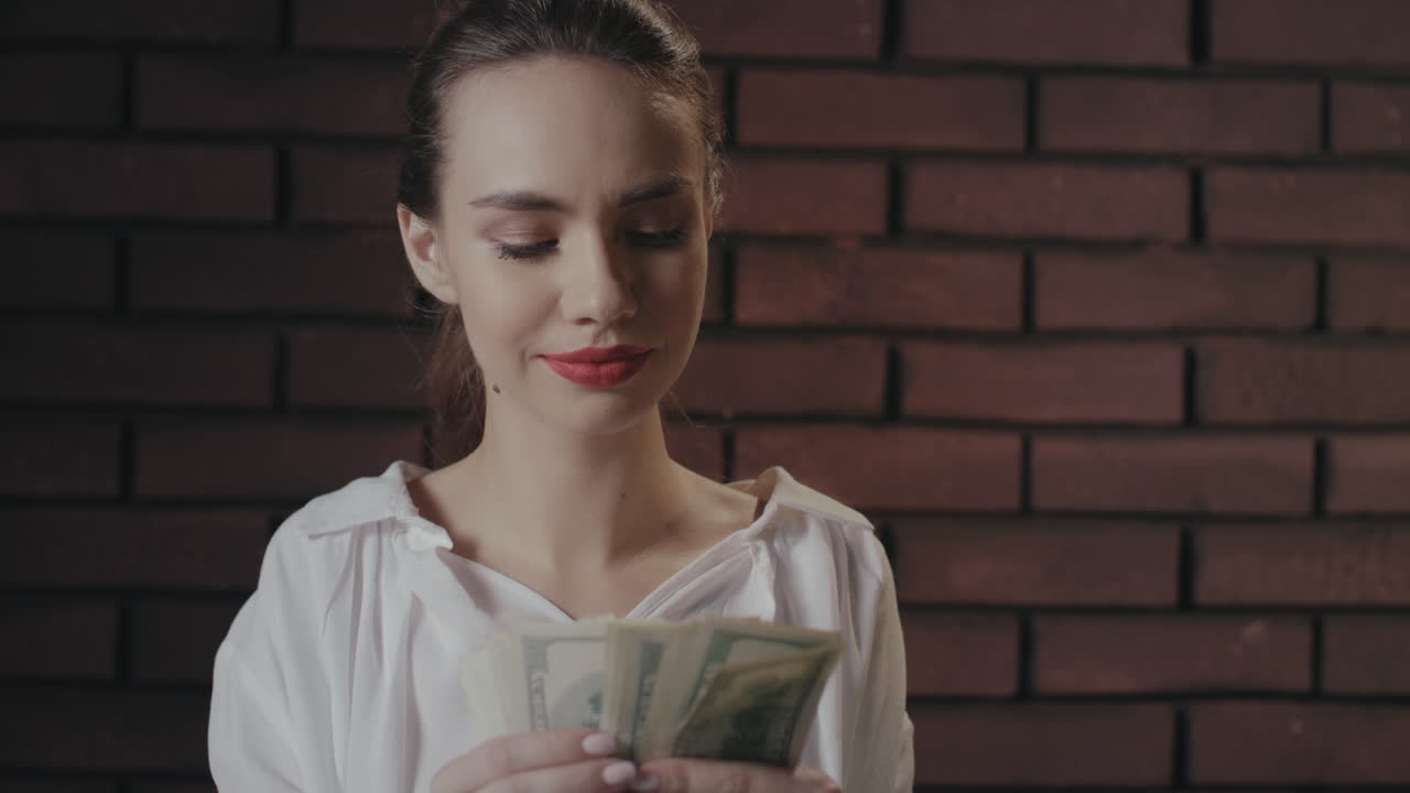 Cheerful business woman counting money for profitable investments on brick wall