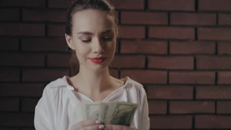 cheerful business woman counting money for profitable investments on brick wall
